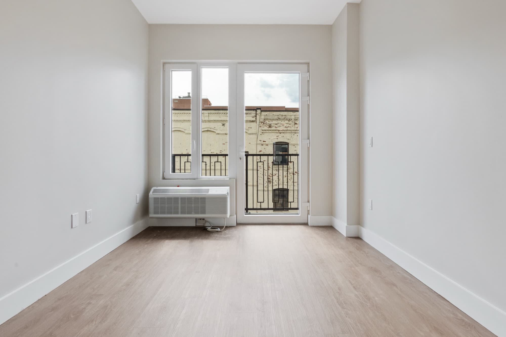 A two-bedroom at The Astelle with full-height balcony doors opening onto a brick Mott Haven streetscape
