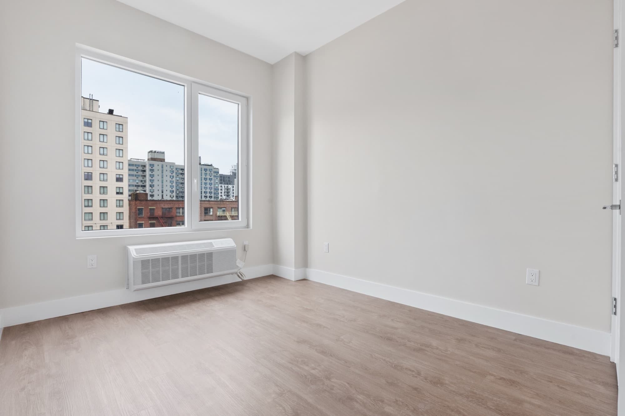 A sunlit Astelle bedroom with oversized windows looking out over the South Bronx